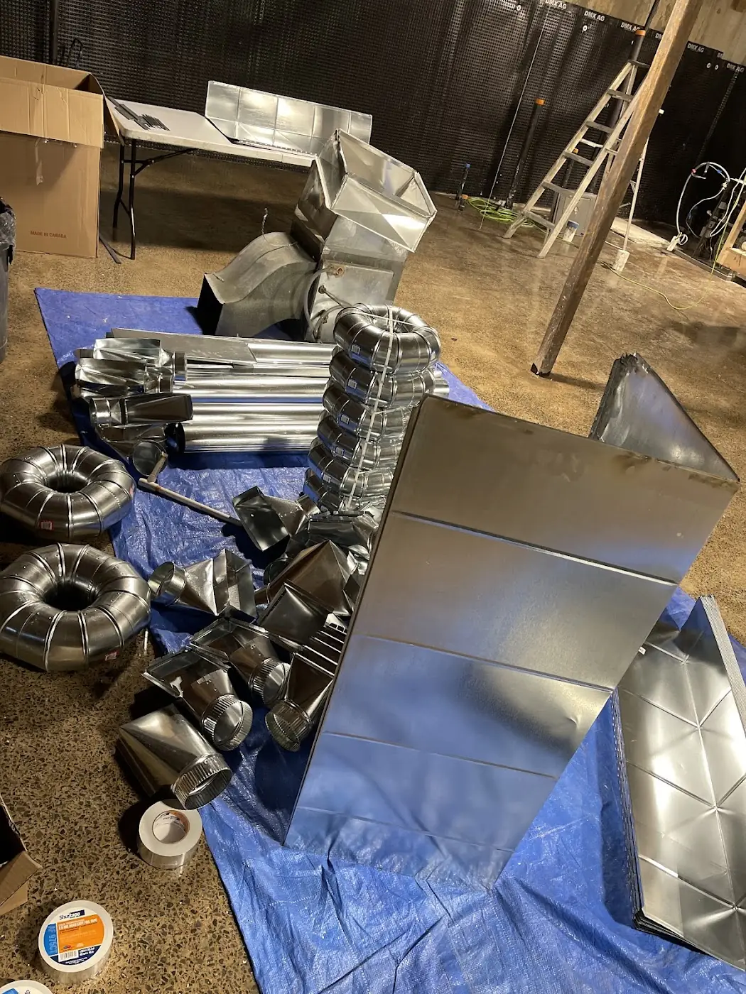 Galvanized duct sections and elbows laid out on a blue tarp